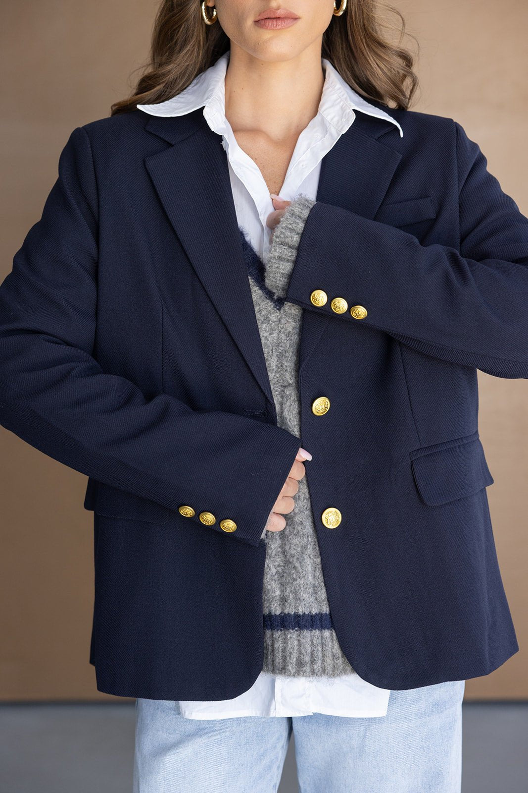 אישה עם ז'קט בלייזר כחול כהה עם כפתורי זהב, סוודר אפור וחולצה לבנה, לוק אופנתי לנשים