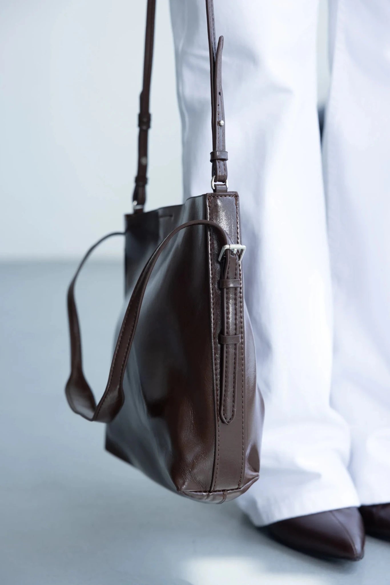 תיק צד חום לנשים עם רצועה מתכווננת, אופנתי על רקע בגדים לבנים ונעליים חומות