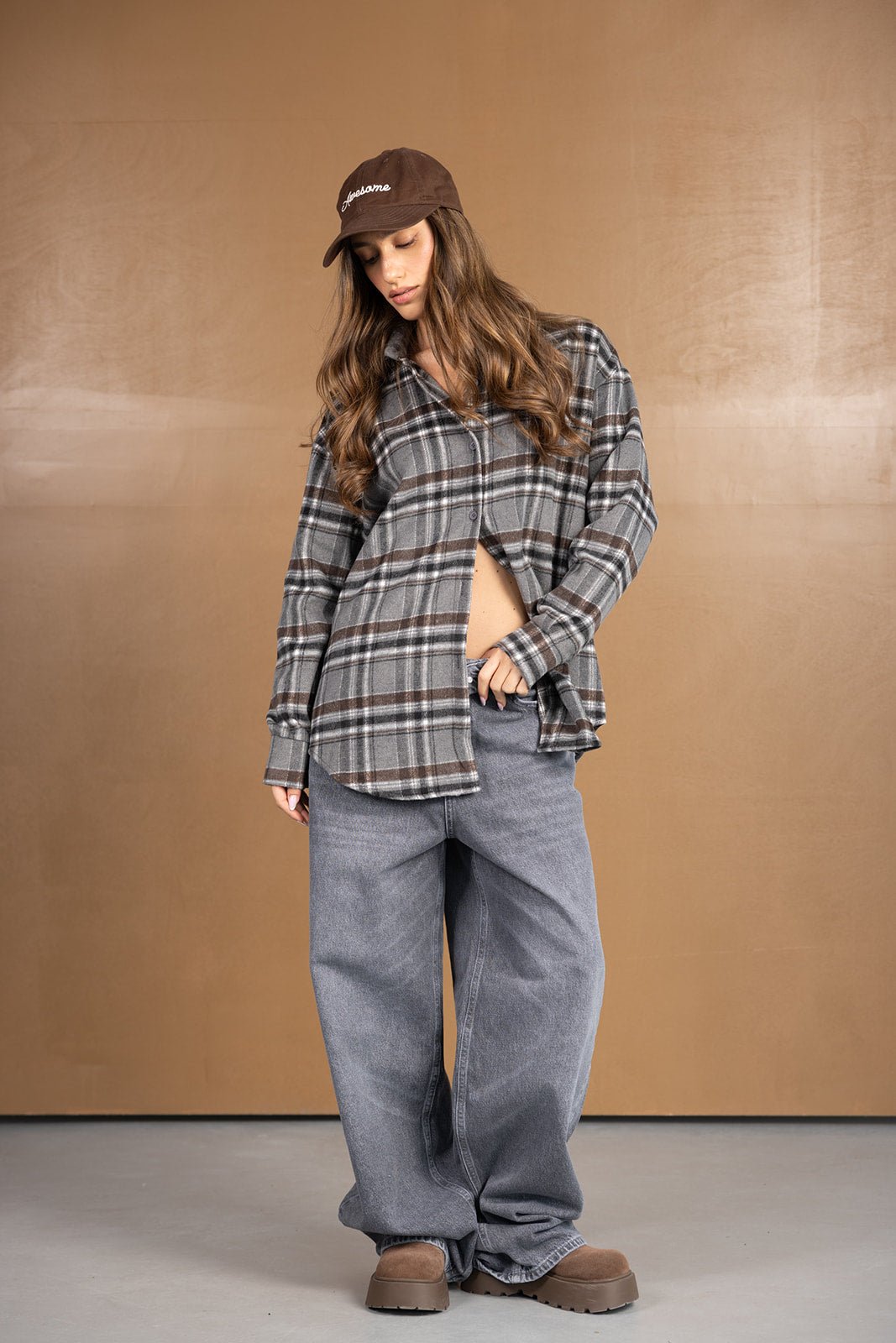 דוגמנית לובשת חולצת פלנל משובצת בגווני אפור וחום, מכנסי ג'ינס רחבים וכובע קפטן חום אופנתי