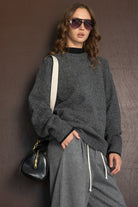 אישה עם סווטשירט אפור, מכנסיים אפורים, משקפי שמש ותיק שחור, לוק אופנתי לנשים