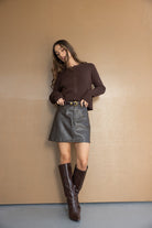 דוגמנית לובשת חצאית דמוי עור שחורה, סוודר חום ומגפיים גבוהים חומים, אופנה לנשים