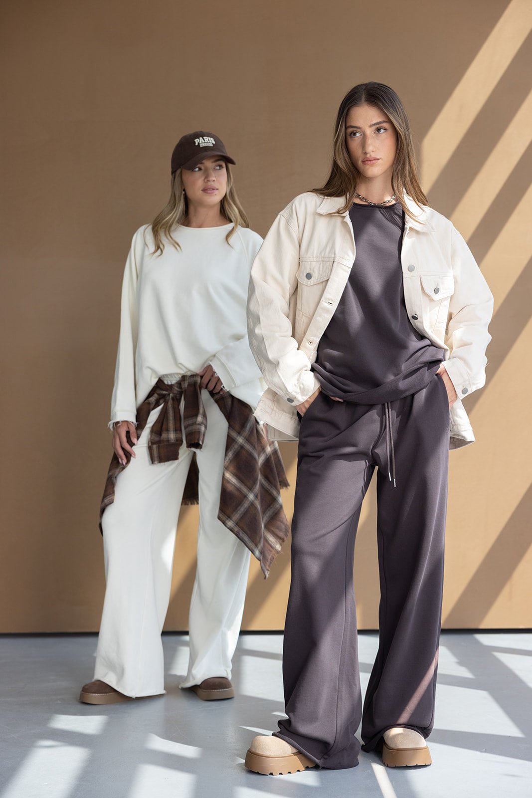 שתי נשים עם בגדי פנאי אופנתיים, אחת בחליפה כהה וג'קט בז', השנייה בלבן עם חולצה משובצת קשורה למותניים