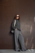 אישה לובשת בגדי אופנה לנשים, סווטשרט אפור ומכנסיים רחבים, משקפי שמש ותיק יד שחור