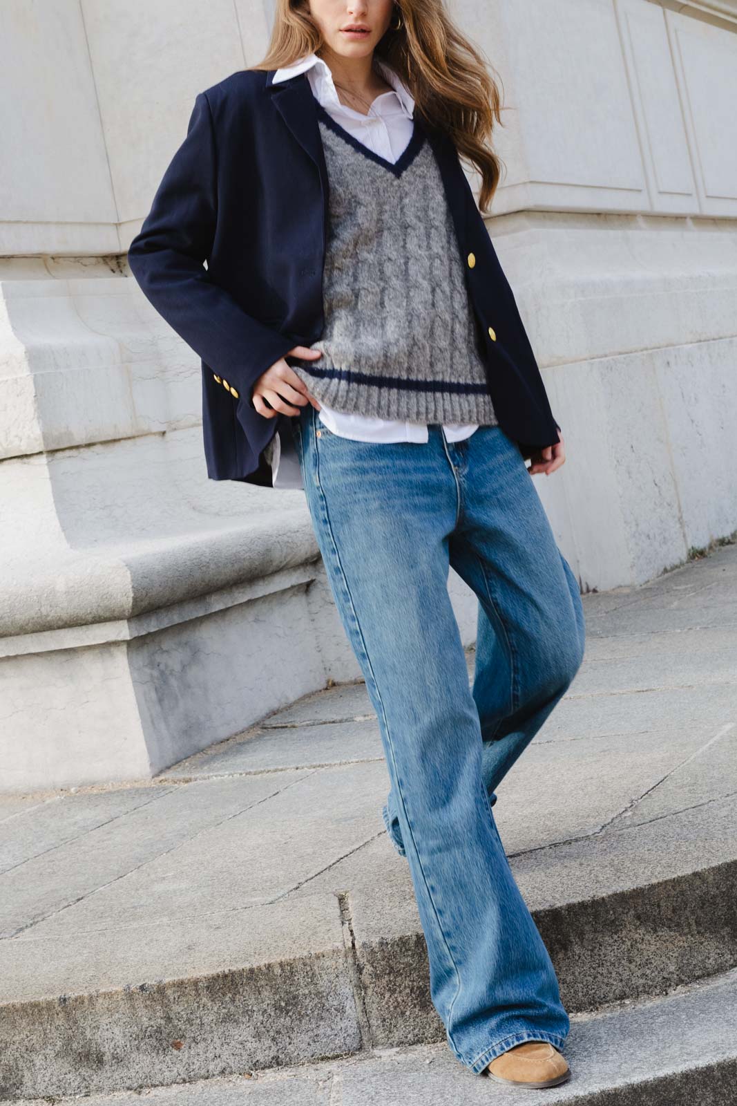 אישה לובשת ג'ינס רחב, חולצה לבנה, סוודר אפור וז'קט כחול, אופנה לנשים ברחוב עירוני