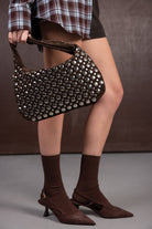 תיק חום עם ניטים כסופים, נעלי עקב חומות וגרביים חומות, חצאית קצרה וחולצה משובצת לאופנת נשים צעירה