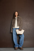 אישה לובשת מעיל חום קצר, סוודר בהיר, ג׳ינס רחב ונעליים חומות ומחזיקה תיק אופנתי