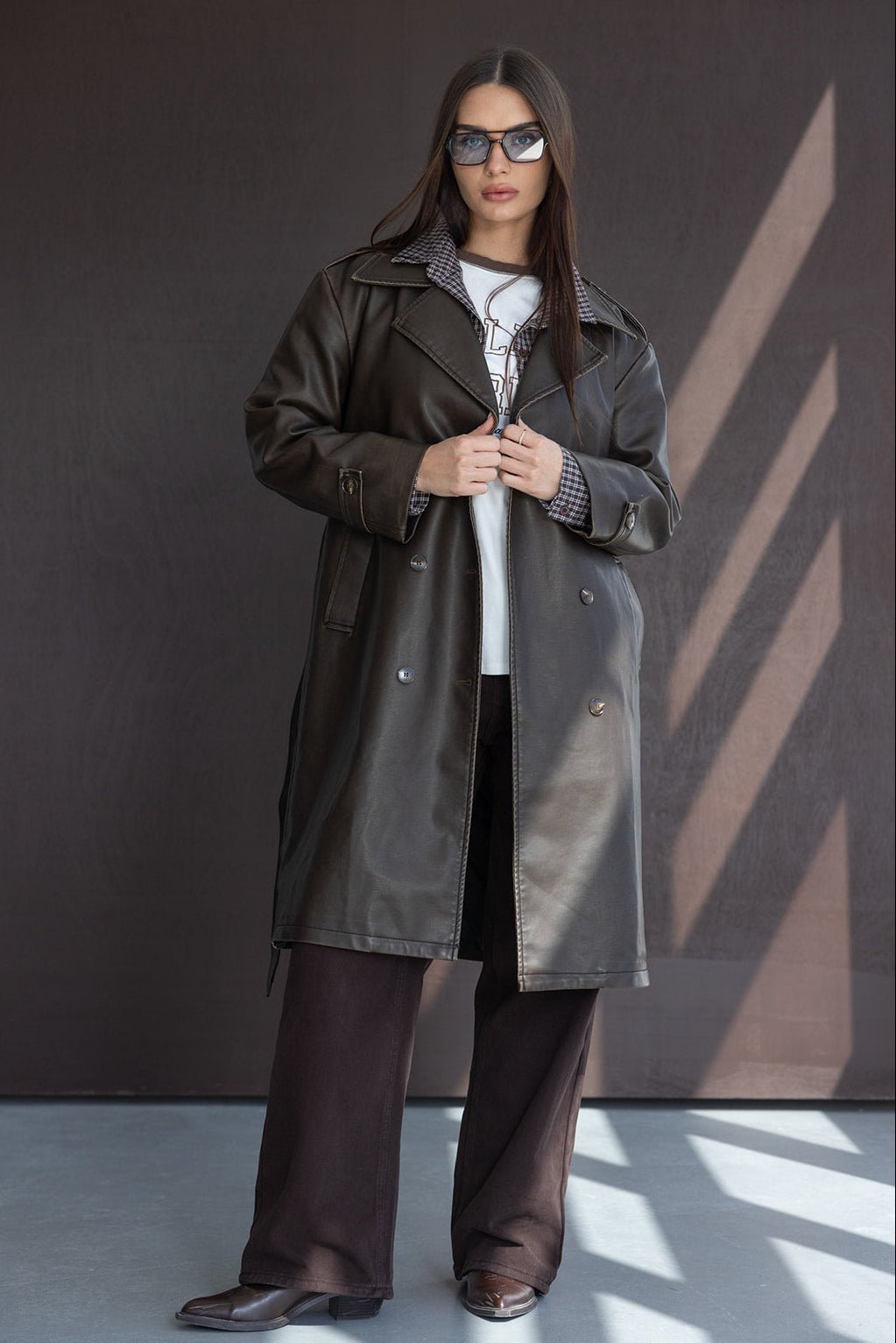 אופנת נשים חורפית, דוגמנית עם מעיל עור שחור ארוך, מכנסיים רחבים ומשקפי שמש
