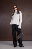 אישה עם קרדיגן אפור פרוותי, מכנסיים שחורים רחבים, משקפי שמש ותיק שחור אופנתי