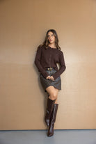 אישה לובשת חולצת כפתורים חומה, חצאית עור חומה ומגפיים גבוהים לאופנת נשים עדכנית