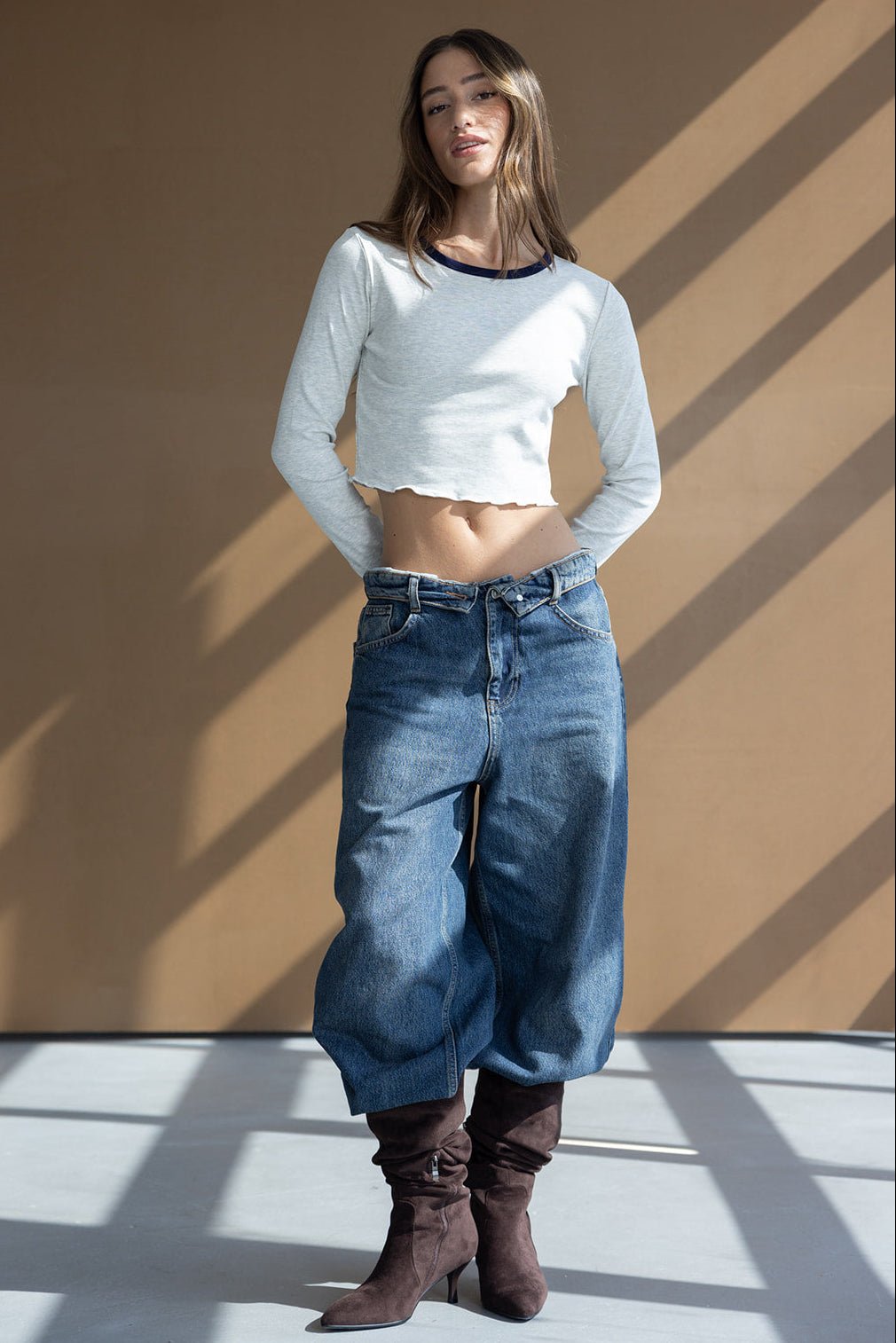 דוגמנית לובשת חולצת קרופ לבנה עם שרוולים ארוכים, ג'ינס רחב בסגנון אופנתי ומגפיים חומים גבוהים