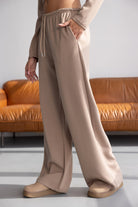 מכנסיים רחבים בצבע בז' לנשים, גזרה גבוהה, בד נוח, מצולמים ליד ספה חומה