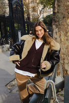 אישה צעירה עם מעיל עור עם פרווה, מכנסי קטיפה חומות וקרדיגן, אופנה רחוב סתווית לנשים