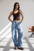 דוגמנית לובשת גופיית נשים חומה עם מכנסי ג'ינס רחבים ונעלי פלטפורמה חומות, אופנה צעירה