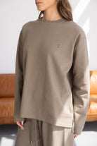 אישה לובשת חולצת טרנינג חומה עם שרוולים ארוכים, סגנון קז'ואל, רקמת לוגו קטנה בחזה