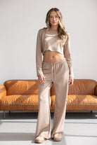 דוגמנית בלבוש סט טרנינג נשים בצבע בז', חולצה ארוכה וקצרה, מכנסיים רחבים, רקע סלון מודרני