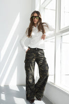 אישה לבושה חולצה לבנה עם כפתורים ומכנסי קארגו רחבים דמוי קאמו, משקפי שמש ירוקים, אופנה לנשים