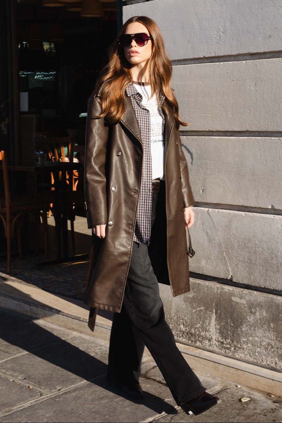 אישה צעירה בלבוש אופנתי, מעיל עור חום, חולצה לבנה, משקפי שמש, רחוב עירוני