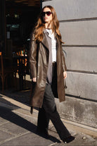 אישה צעירה בלבוש אופנתי, מעיל עור חום, חולצה לבנה, משקפי שמש, רחוב עירוני