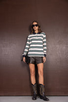 אישה עם חולצת פסים ארוכה, מכנסי עור קצרים, מגפי בוקרים ומשקפי שמש, לוק אופנתי לנשים