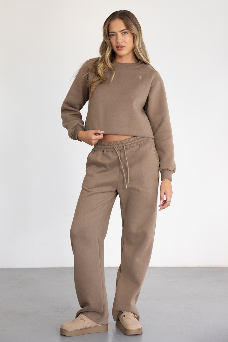 דוגמנית לובשת סט טרנינג נשים חום עם מכנסיים רחבים וסווטשירט בגזרה מחויטת, אופנת חורף
