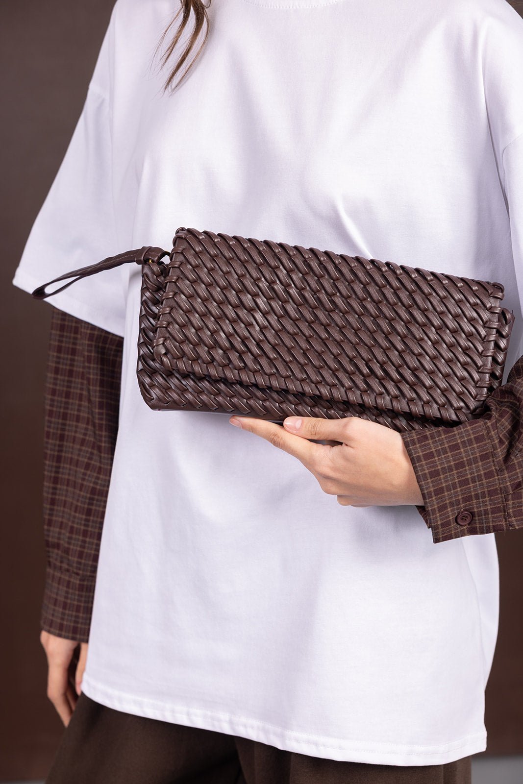 אישה מחזיקה תיק קלאץ' קלוע חום, חולצה לבנה עם שרוולים משובצים, אופנה לנשים