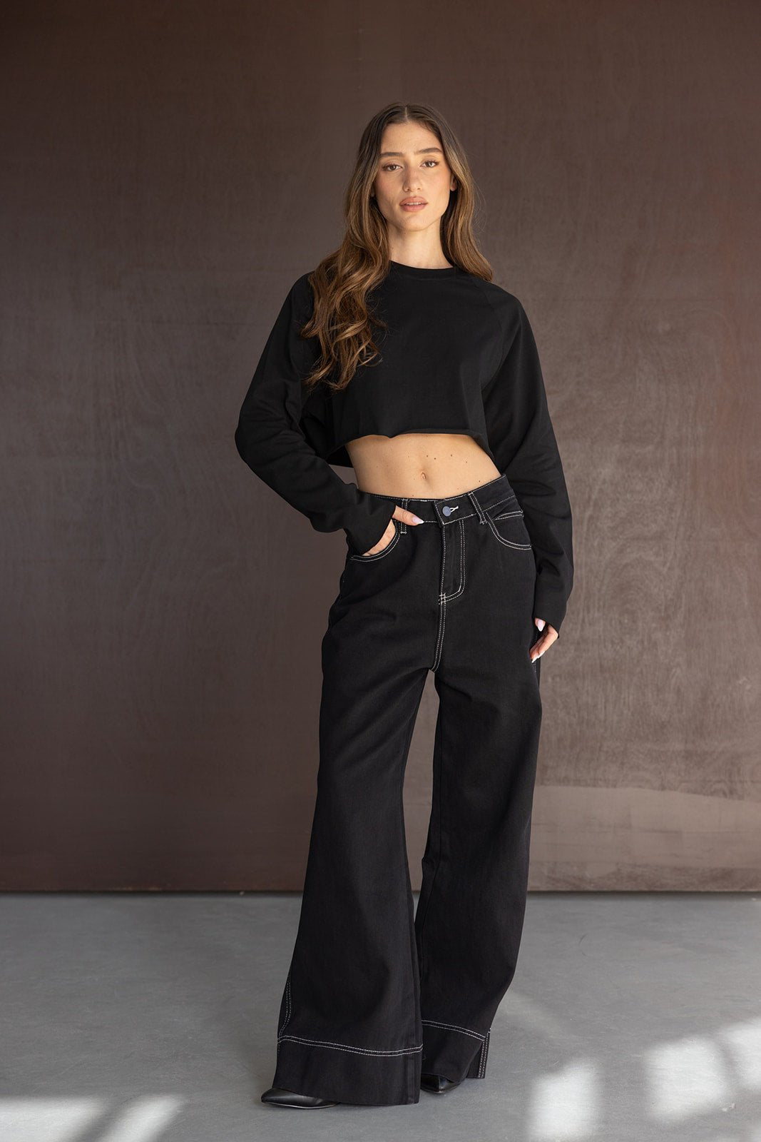 אישה לובשת חולצת קרופ שחורה ומכנסיים שחורים רחבים עם תפרים לבנים, בגדי אופנה לנשים