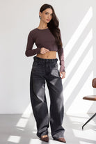 אישה לובשת חולצת קרופ ארוכה בצבע חום כהה עם ג'ינס שחור רחב, אופנת נשים עדכנית