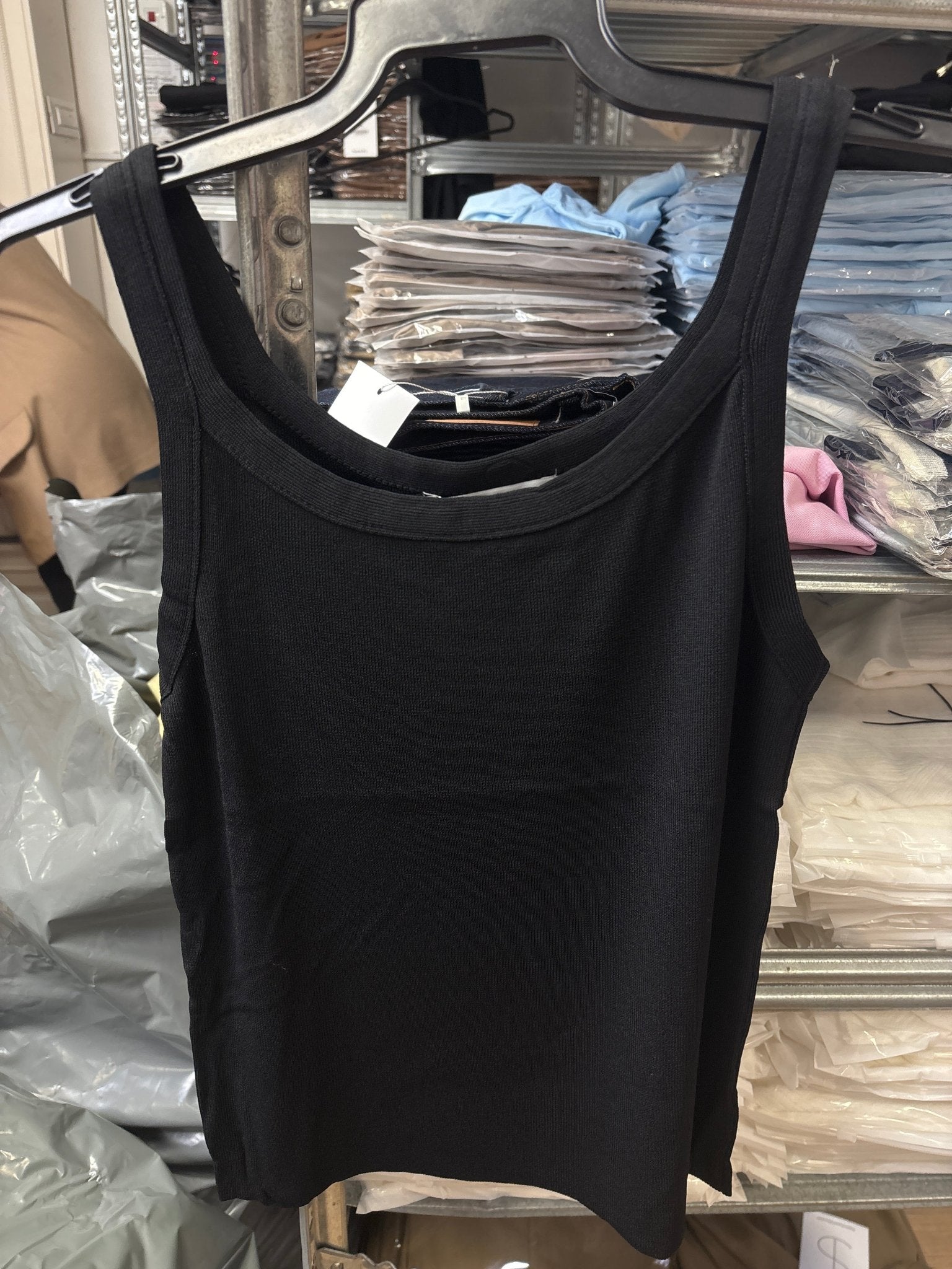 גופיה basic שחורה לנשים תלויה על קולב בחנות בגדים, רקע של מדפים עם בגדים מקופלים