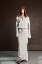 דוגמנית עם שמלת סווטשירט אפורה ארוכה, כובע קפטן חום ונעלי פלטפורמה, צילומי אופנה ברקע חום