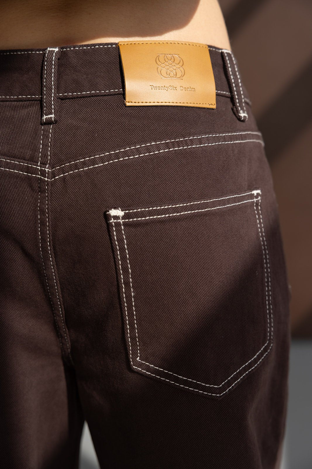 ג׳ינס נשים חום עם תפרים לבנים ותווית עור על המותן, אופנה לנשים צעירות