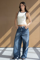 דוגמנית עם גופיה לבנה שולי כחול ומכנסי ג'ינס רחבים, אופנת נשים טרנדית