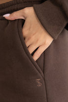 תקריב על כיס מכנסי ספורט נשים בצבע חום עם יד בתוך הכיס ורקמת ראשי תיבות אופנתית