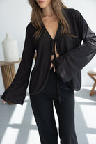 אישה לובשת חולצה שחורה עם שרוך קשירה ומכנסיים מחויטים שחורים, אופנת נשים מודרנית