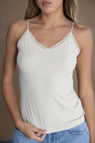 גופיית נשים לבנה עם כתפיות דקות ותחרה, על דוגמנית עם ג'ינס, אופנת קיץ לנערות