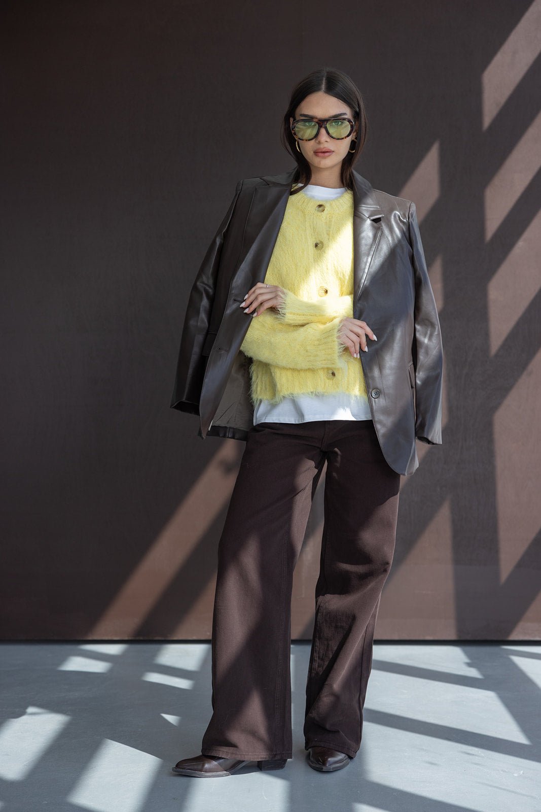 אישה עם קרדיגן פרווה צהוב, בלייזר עור חום, מכנסיים כהים ומשקפי שמש אופנתיים, לוק חורפי לנשים
