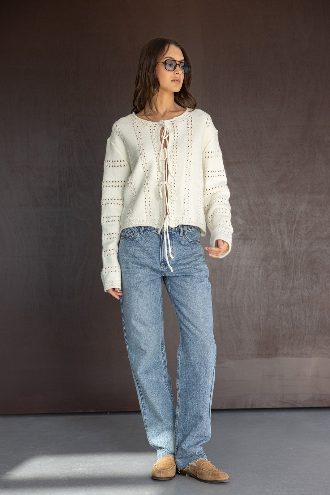 אישה עם סוודר לבן סרוג עם שרוכים, ג'ינס רחב ונעלי זמש חומות, לוק אופנתי לצעירות