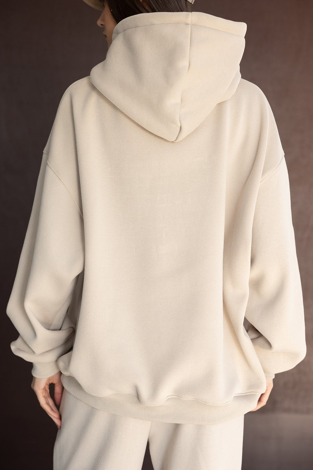 אישה לובשת סט טרנינג בגוון בז', קפוצ'ון ומכנסיים רחבים, צילום מגב