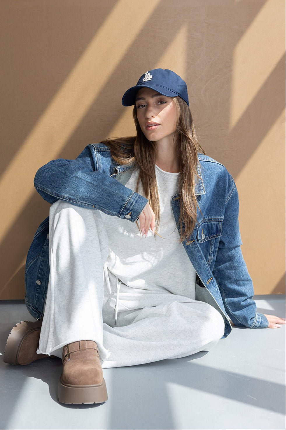 אישה יושבת עם ז'קט ג'ינס, כובע כחול, סווטשירט אפור ומגפיים חומים אופנתיים לצעירות