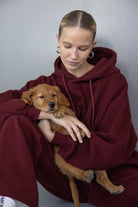 אישה בלבוש טרנינג בורדו מחבקת גור כלבים חום, אופנת נשים חורף נוחה וסטייליסטית