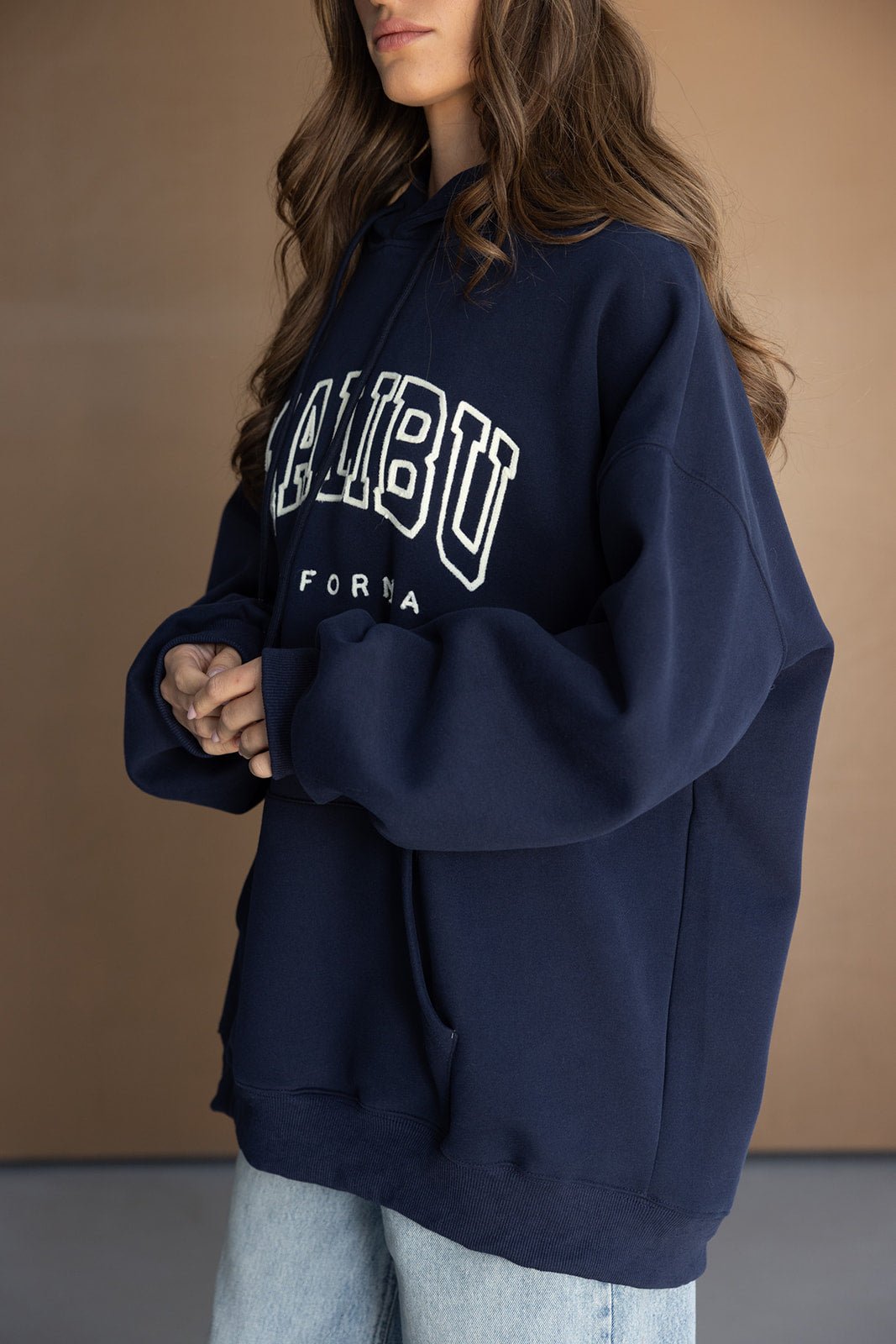 אישה לובשת קפוצ'ון אוברסייז כחול כהה עם כיתוב 'Malibu' ומכנסי ג'ינס בהירים, אופנת רחוב לנשים