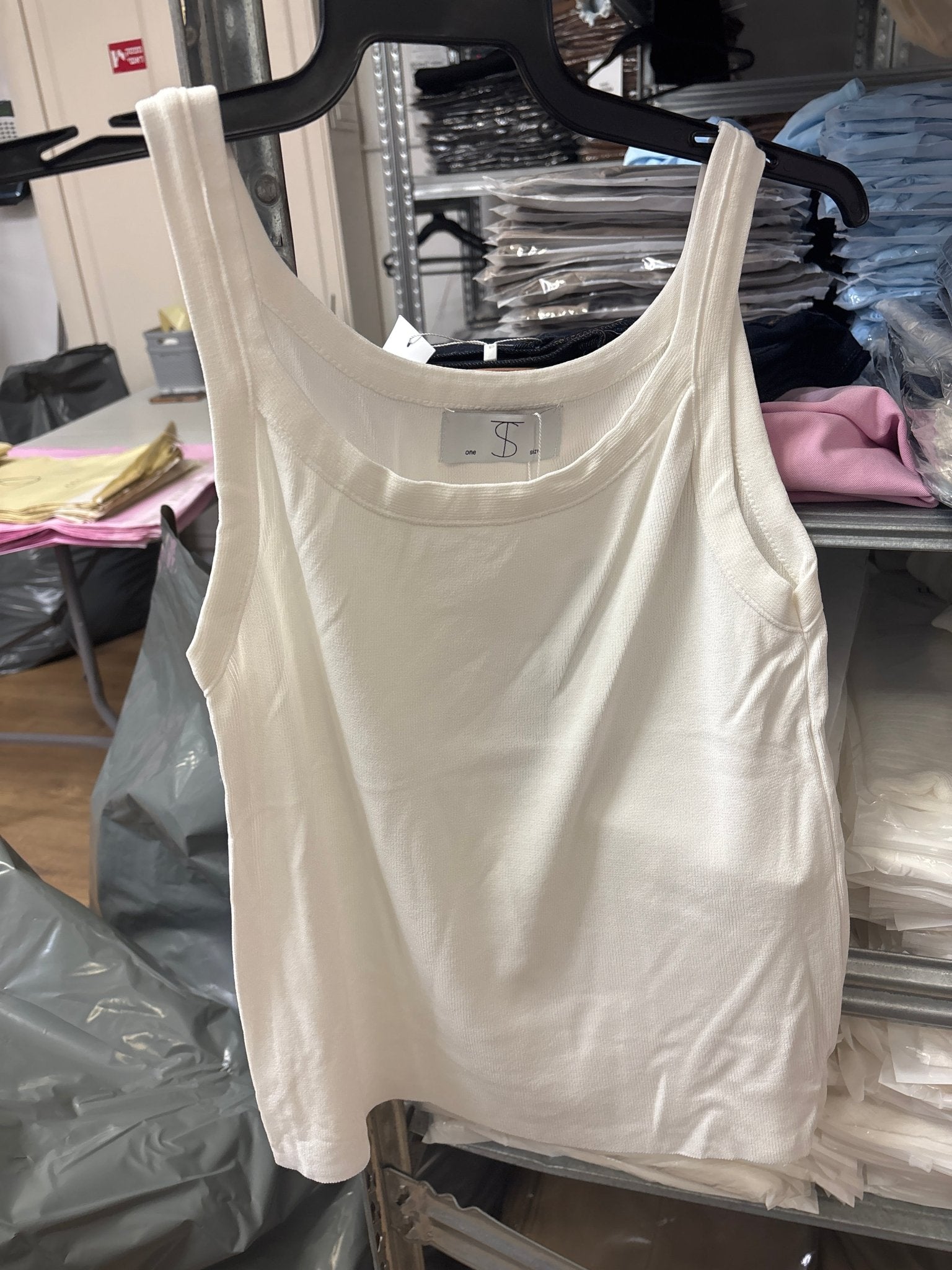 גופיה לבנה לנשים עם כתפיות רחבות על קולב, רקע מדפי בגדים בחנות אופנה