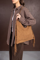 אישה לובשת חולצת משבצות חום ונושאת תיק כתף חום עם קליעה ופרנזים, אופנת נשים עדכנית