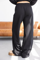 מכנסי נשים שחורים בגזרה רחבה וקומות גבוה, שיק נינוח ליד ספה עור חומה