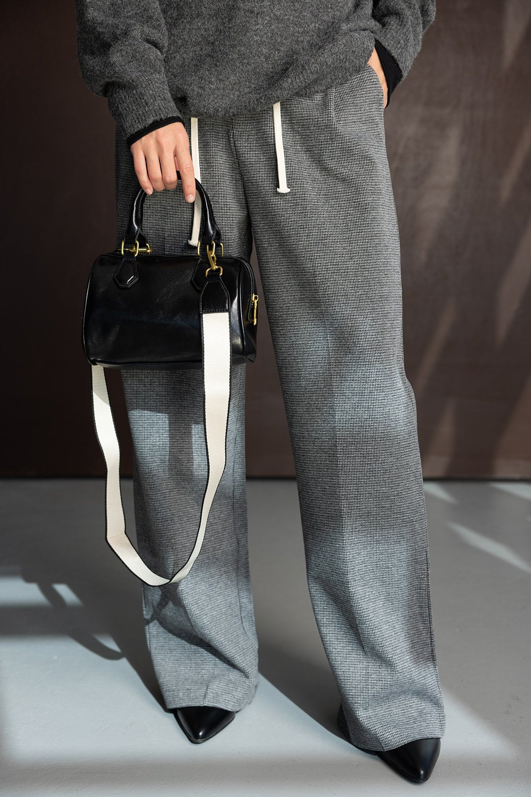 מכנסיים רחבים לנשים אפור עם שרוך לבן, סוודר כהה ותיק צד שחור אופנתי