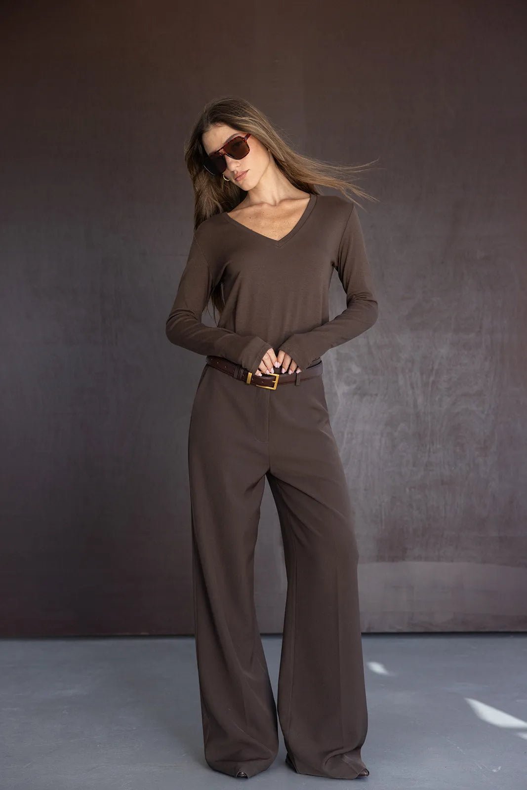 אישה לובשת סט חום אופנתי עם מכנסיים רחבים וחולצה ארוכה, משקפי שמש טרנדיים, אופנת נשים