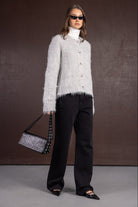 אישה עם קרדיגן פרוותי אפור, מכנסיים שחורים, גולף לבן, משקפי שמש ותיק כתף שחור, אופנת נשים חורף