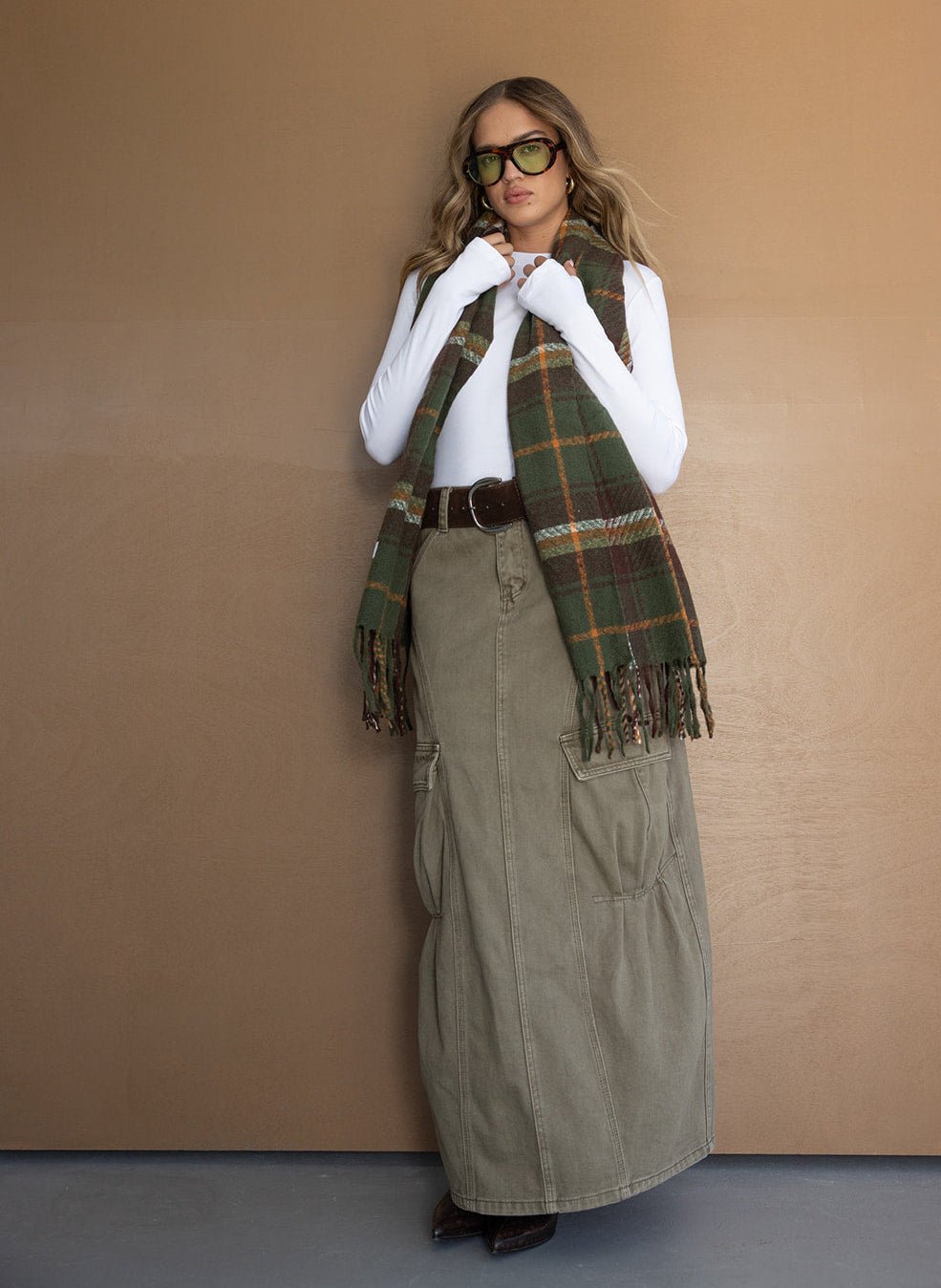 אישה עם חולצה לבנה ארוכה, חצאית cargo ירוקה, צעיף משובץ ומשקפי שמש אופנתיות