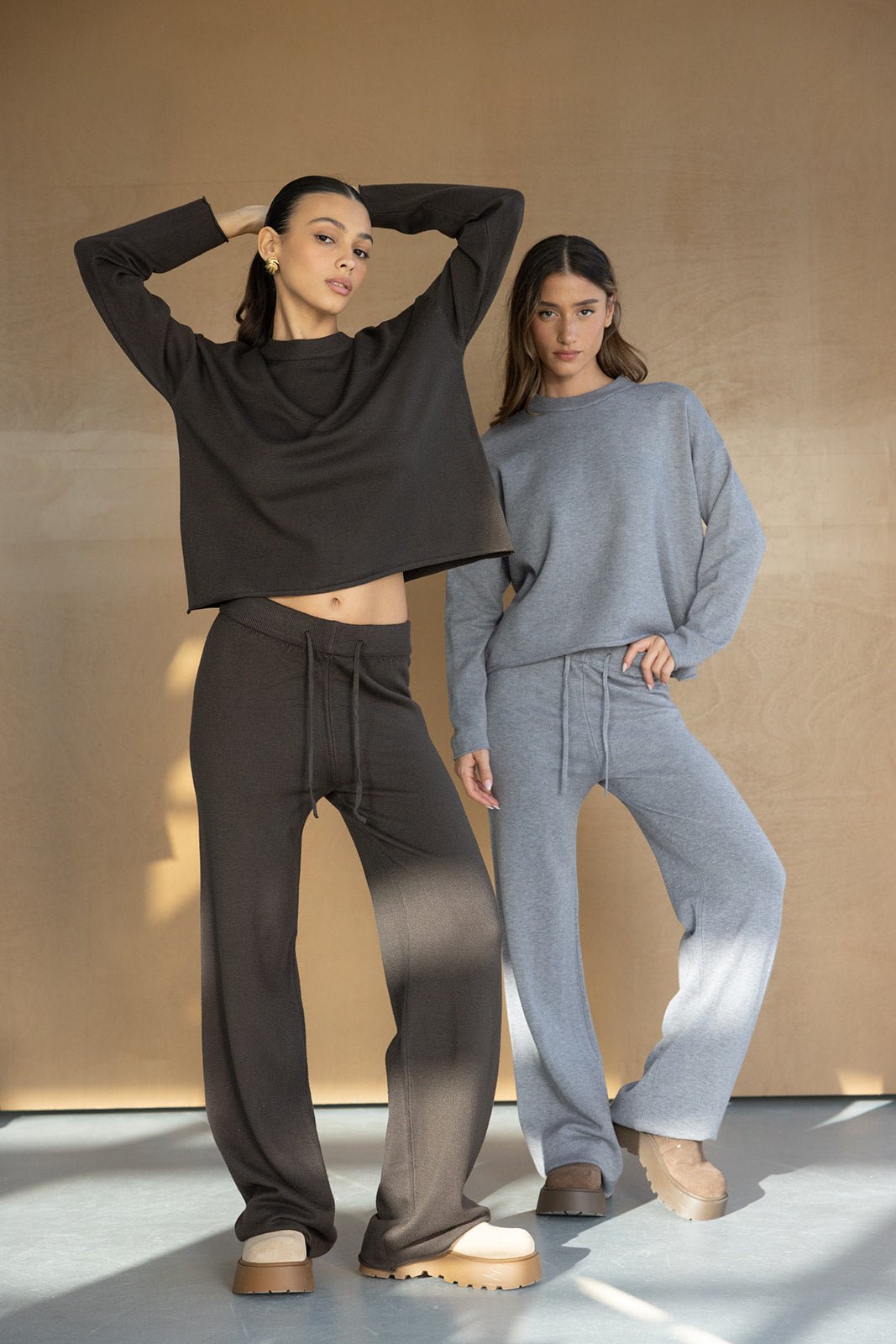 שתי נשים מדגימות סט טרנינג אופנתי בצבעים שחור ואפור עם מגפיים, אופנת סתיו חורף לנערות