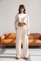 דוגמנית עם סט טרנינג בגוון בז', מכנסיים רחבים וחולצה קרופ, כובע מצחייה, יושבת על ספה חומה בסגנון מודרני