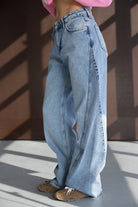 ג'ינס רחב לנשים בגזרה גבוהה בגוון תכלת משופשף, משולב סווטשירט ורוד ונעלי סניקרס חומות